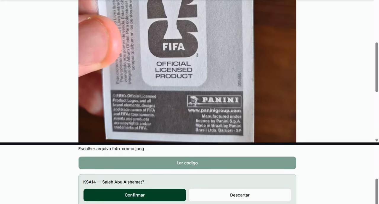 Foto tirada à mão do verso de uma figurinha Panini, com os dizeres de licença e um número de série impresso na lateral; abaixo, a resposta do app propondo o cromo KSA14, Saleh Abu Alshamat, com os botões Confirmar e Descartar.